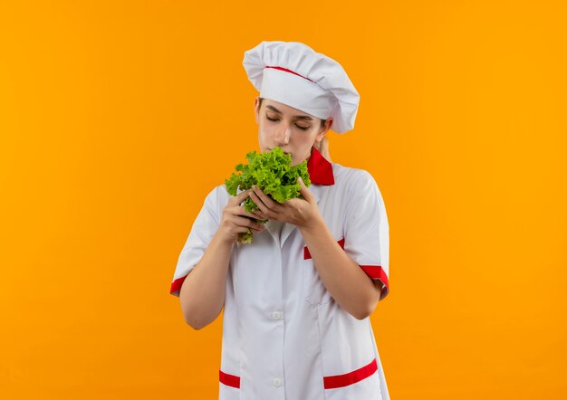 Junge hübsche Köchin in der Kochuniform, die Salat hält und schnüffelt