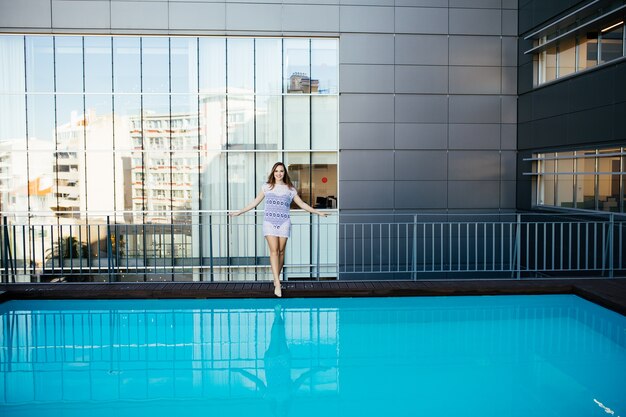 Junge hübsche Modesportfrau, die im Sommer im Freien in heißem Wetter im Bikini auf Pool aufwirft