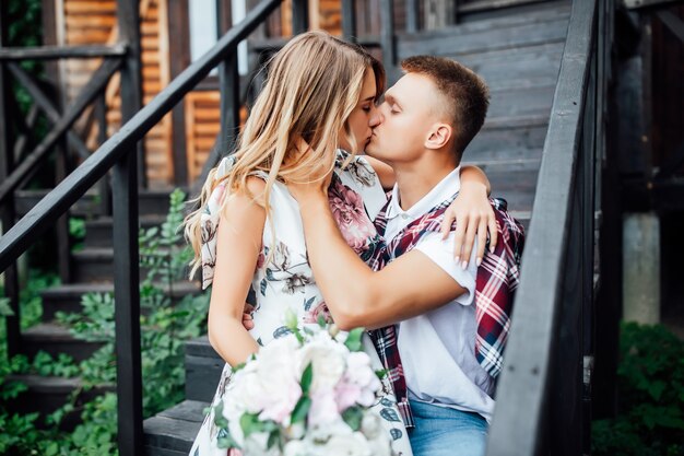 Junge hübsche Paare, die sich in der Nähe des neuen Holzhauses küssen und den Tag ihrer Hochzeit feiern. Liebesgeschichte.