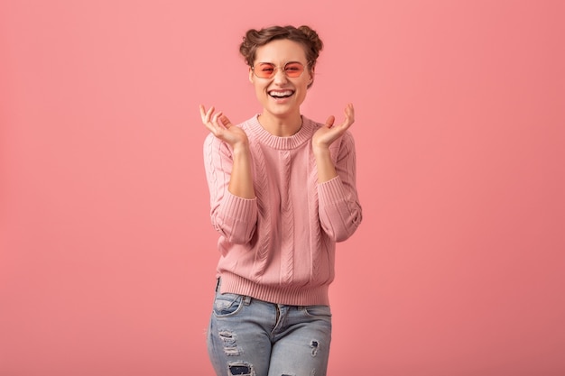 Junge hübsche verlassene lachende frau im rosa pullover und in der sonnenbrille lokalisiert auf rosa studiohintergrund