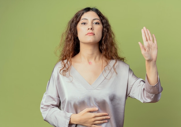 junge hübsche weibliche Büroangestellte, die Hand auf Bauch legt und Stoppgeste zeigt, die auf olivgrüner Wand lokalisiert wird