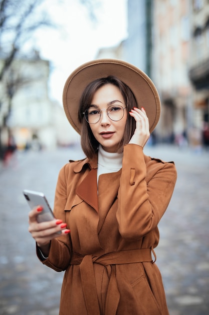 Junge im breiten Hut, der SMS auf Smartphone-Herbststraße schreibt