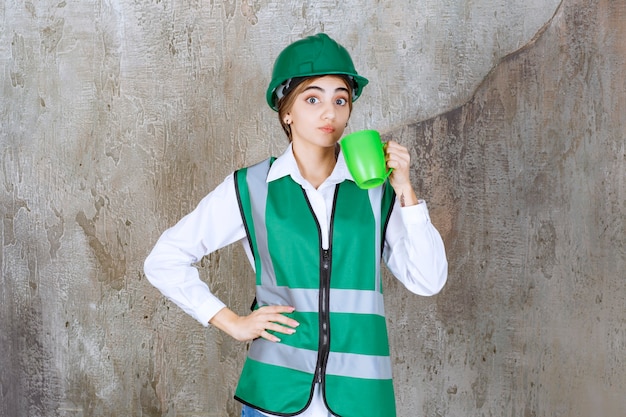 Junge Ingenieurin, die eine grüne Weste trägt und eine Kaffeetasse hält