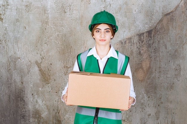 Junge Ingenieurin in grüner Weste und Helm mit Papierkasten