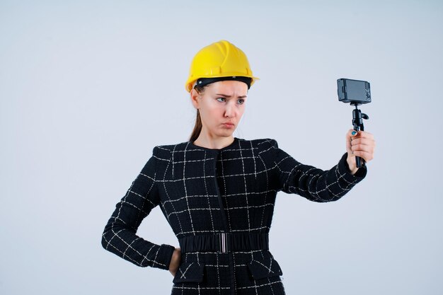 Junge Ingenieurin macht Selfie mit ihrer Kamera, indem sie traurige Mimikry auf weißem Hintergrund zeigt