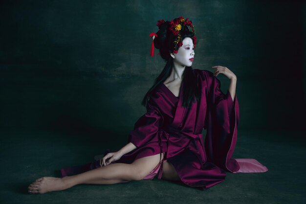 Junge japanische Frau als Geisha auf dunkelgrünem Hintergrund. Retro-Stil, Vergleich des Epochenkonzepts.