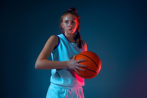 Junge kaukasische Basketballspielerin auf blauem Studiohintergrund in Neonlicht, Bewegung und Aktion.