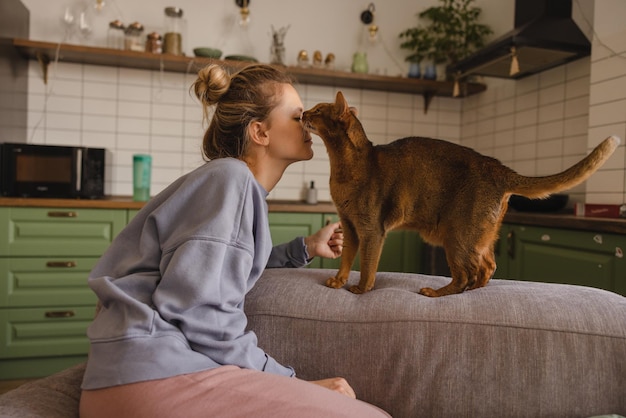 Junge kaukasische blonde Frau mit Freizeitkleidung ist in Kontakt mit Katze, während sie auf der Couch sitzt Haustierkonzept