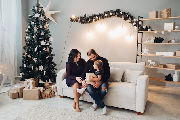 Junge kaukasische dreiköpfige Familie sitzt zusammen auf dem Sofa neben dem Weihnachtsbaum