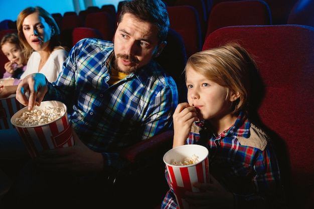 Junge kaukasische Familie, die einen Film in einem Kino, Haus oder Kino sieht. Sieh ausdrucksstark, erstaunt und emotional aus. Allein sitzen und Spaß haben. Beziehung, Liebe, Familie, Kindheit, Wochenendzeit.