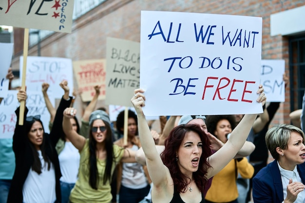 Kostenloses Foto junge kaukasische frau, die ein banner trägt, während sie mit menschenmassen an öffentlichen demonstrationen teilnimmt