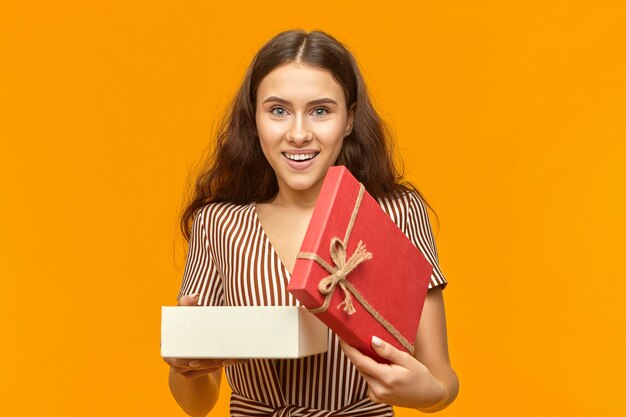 junge kaukasische Frau mit dem langen lockigen Haar lächelnd, das ein geöffnetes Geschenk hält