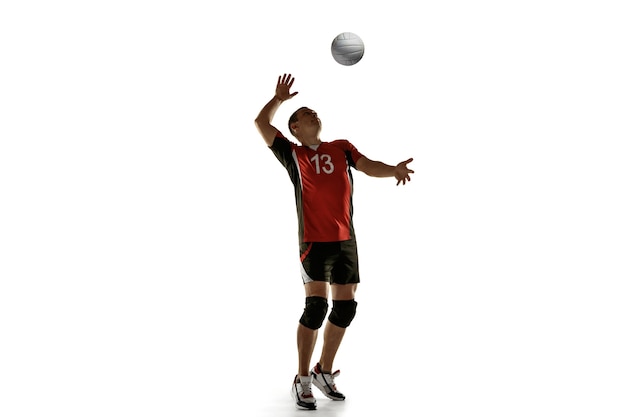 Junge kaukasische Volleyballspielerin, die isoliert auf weißer Wand praktiziert Männliches Sportlertraining mit dem Ball in Bewegung und Aktion. Sport, gesunder Lebensstil, Aktivität, Bewegungskonzept. Exemplar.