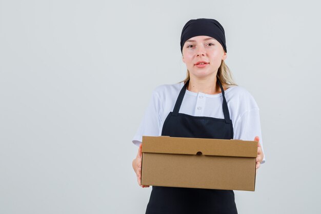 Junge Kellnerin hält Pappkarton in Uniform und Schürze