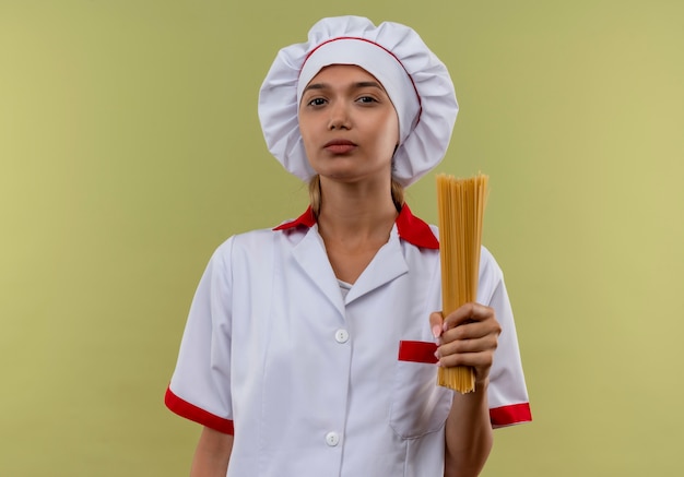 junge Kochfrau, die Kochuniform trägt, die Spaghetti auf isolierter grüner Wand mit Kopienraum hält