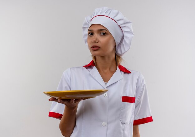 junge Köchin, die Kochuniform trägt, hält Platte auf isolierter weißer Wand mit Kopienraum