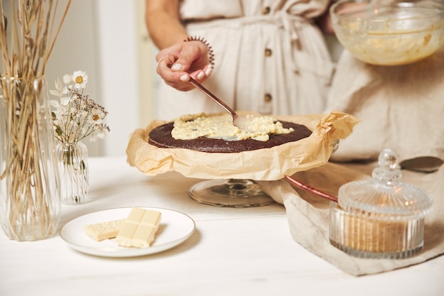 Junge Köchin macht einen köstlichen Schokoladenkuchen mit Sahne auf einem weißen Tisch