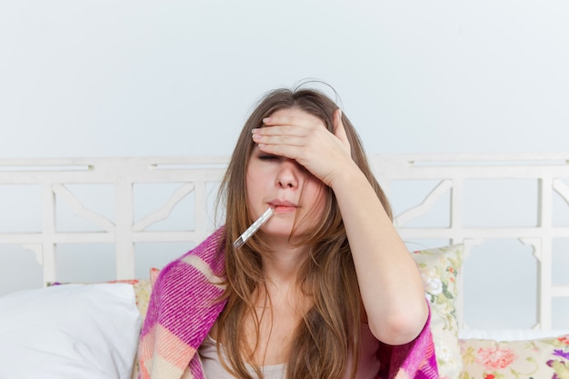 Junge kranke Frau in der Decke mit Thermometer