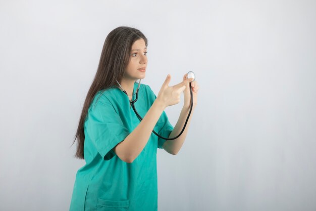 Junge Krankenschwester, die weg schaut und mit dem Finger auf das Stethoskop zeigt.