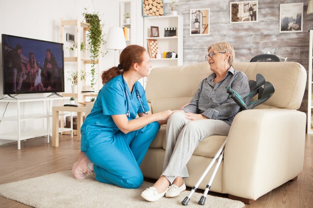 Junge Krankenschwester trägt blaue Uniform im Gespräch mit Seniorin im Pflegeheim.