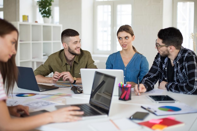 Junge kreative Leute mit Laptop und Notizblock, die in einem modernen Büro arbeiten Coole Jungs diskutieren gemeinsam über neue Projekte, während sie Zeit bei der Arbeit verbringen