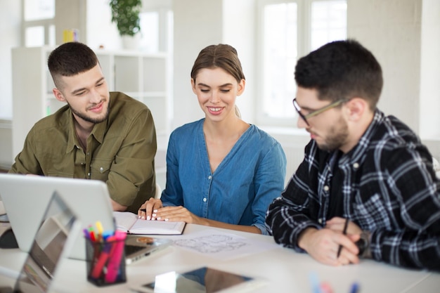 Junge kreative Menschen mit Laptop diskutieren gemeinsam über neue Projekte Gruppe lächelnder Mädchen und Jungen, die in einem modernen Büro arbeiten