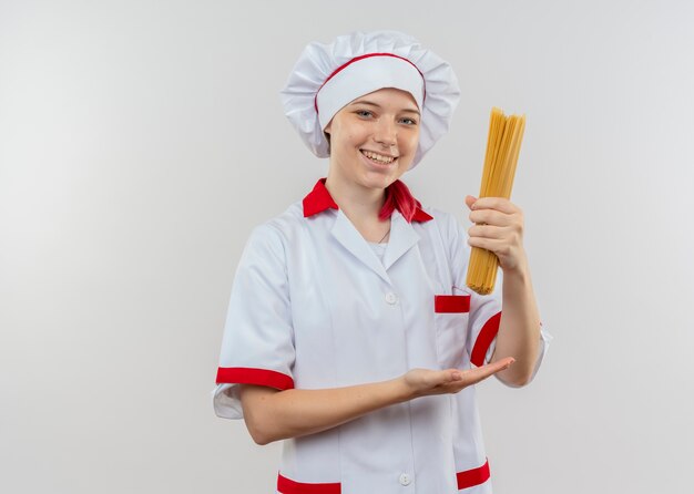 Junge lächelnde blonde Köchin in Kochuniform hält Bündel Spaghetti lokalisiert auf weißer Wand