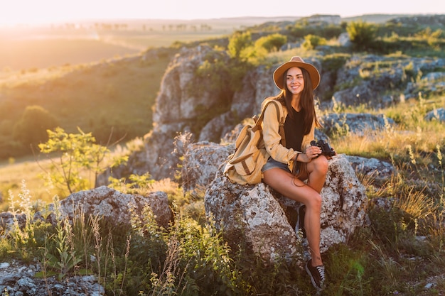 Junge lächelnde Frau, die auf dem Felsen hält binokular sitzt