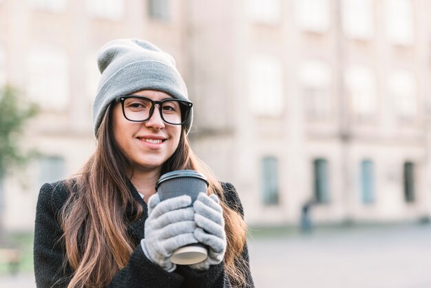 Junge lächelnde Frau, die Cup des Getränks auf Straße hält