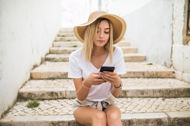 Junge lächelnde Frau, die draußen auf Treppen mit Smartphone sitzt