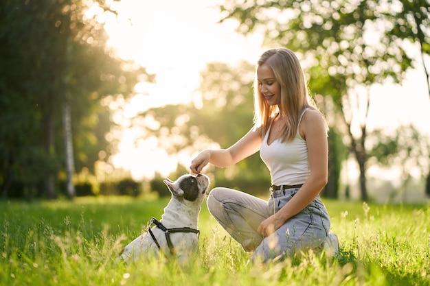 Junge lächelnde Frau, die französische Bulldogge im Park ausbildet