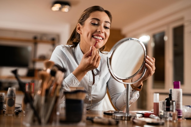 Junge lächelnde Frau, die Lipliner aufträgt, während sie sich im Spiegel betrachtet
