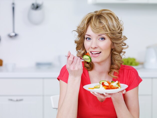 Junge lächelnde Frau, die Salat in der Küche - drinnen isst