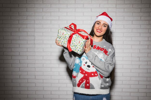 Junge lächelnde Frau im Weihnachtshut und -strickjacke mit Präsentkarton