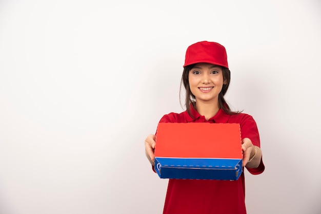 Junge lächelnde Frau in der roten Uniform, die Pizza im Kasten liefert.