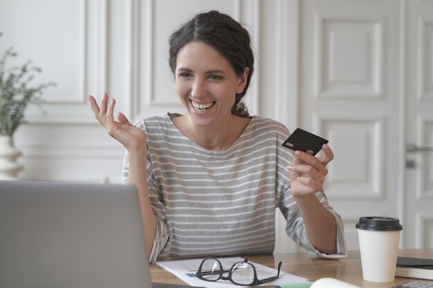 Junge lächelnde italienische frau, die beim online-shopping auf dem laptop mit plastikkarte bezahlt?