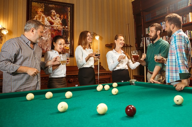 Junge lächelnde Männer und Frauen, die nach der Arbeit Billard im Büro oder zu Hause spielen. Geschäftskollegen, die sich mit Freizeitaktivitäten beschäftigen. Freundschaft, Freizeitbeschäftigung, Spielkonzept.