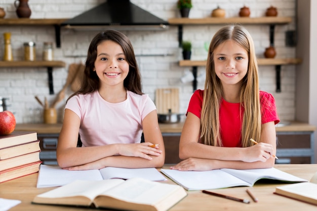 Junge lächelnde Schulmädchen, die am Schreibtisch sitzen und zu Hause trainieren