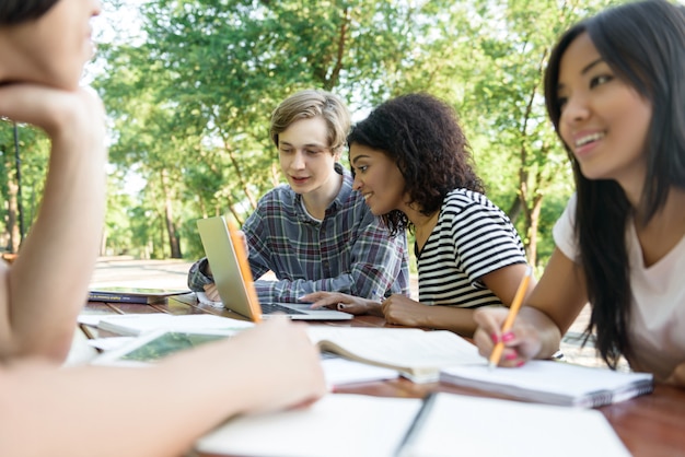 Junge lächelnde Studenten, die draußen sitzen und studieren