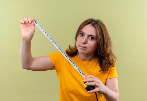 Junge lässige Frau, die Bandmeter und auf isolierter grüner Wand hält