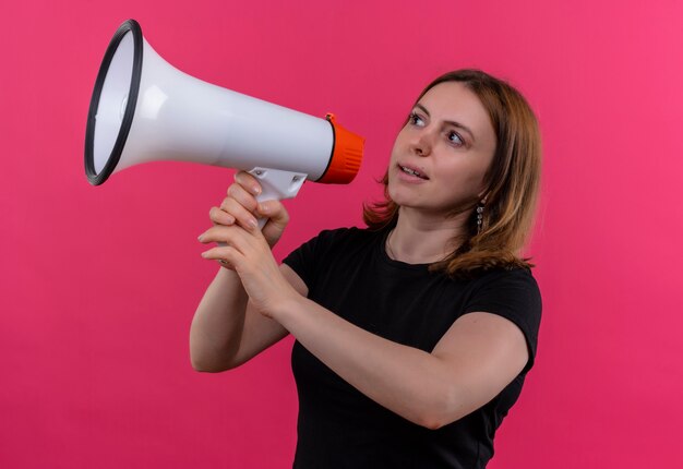 Junge lässige Frau, die durch Sprecher spricht, der linke Seite auf isolierter rosa Wand betrachtet