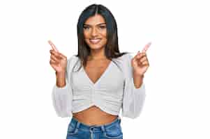 Kostenloses Foto junge lateinamerikanische transsexuelle transgender-frau in lässiger kleidung lächelt selbstbewusst und zeigt mit den fingern in verschiedene richtungen, kopiert platz für werbung