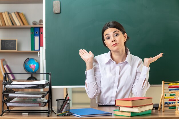 junge Lehrerin sitzt am Tisch mit Schulwerkzeugen im Klassenzimmer