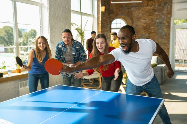 Junge Leute, die am Arbeitsplatz Tischtennis spielen, Spaß haben