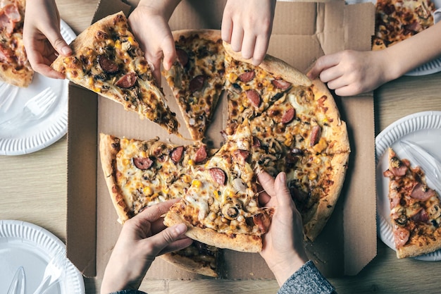 Kostenloses Foto junge leute, die scheiben heißer pizza aus dem karton in der tischansicht nehmen