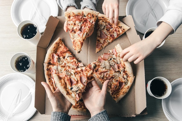 Junge Leute, die Scheiben heißer Pizza aus dem Karton in der Tischansicht nehmen