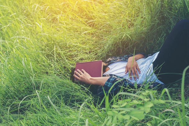 Junge liegt auf dem Rasen mit einem Buch auf dem Gesicht