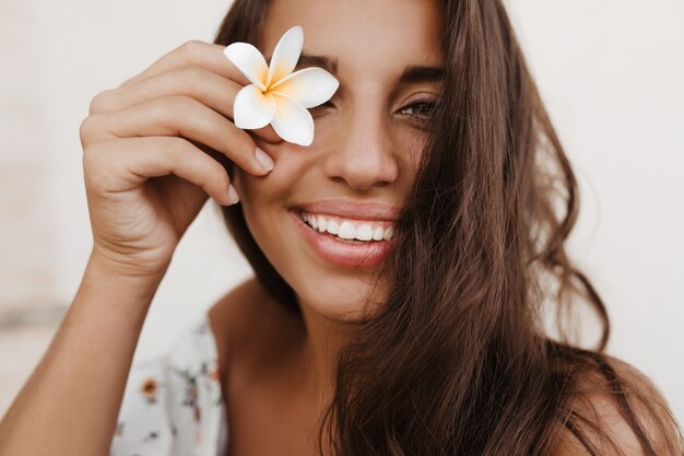 Junge lockige brünette Frau bedeckt ihre Augen mit weißer Blume