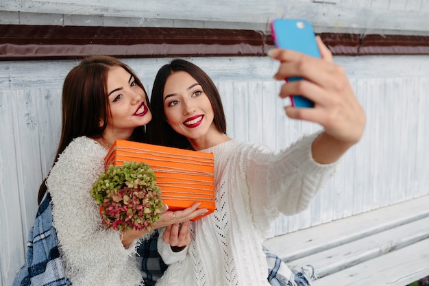 Junge Mädchen, die ein Foto mit einem blauen Handy und einem orange Geschenk nehmen