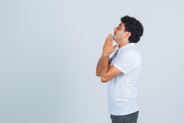 Junge Männer, die Hände in betender Geste in weißem T-Shirt, Hose halten und hoffnungsvoll aussehen. .